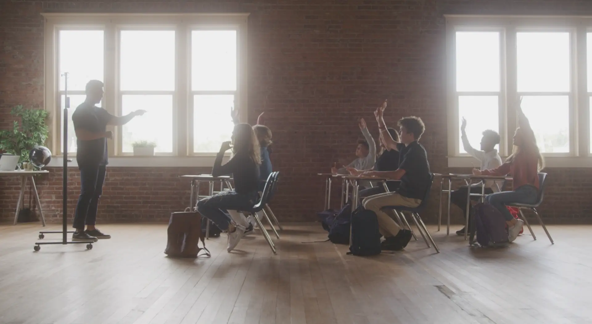 Students in a bright loft-style classroom raising hands and reacting during an interactive school magic show
