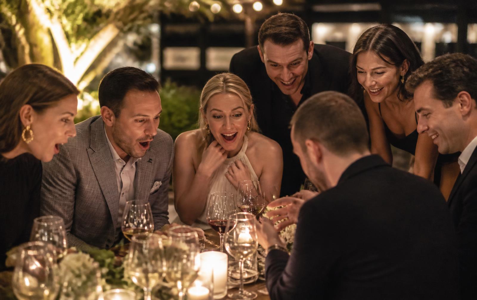 Guests at an evening dinner party leaning in with surprise during close-up magic